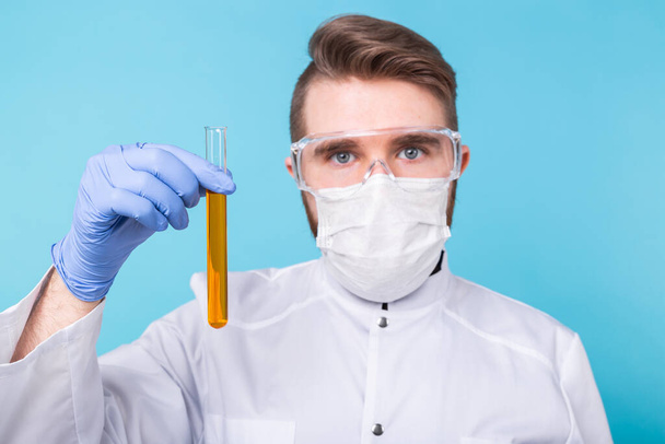 Covid-19, coronavirus, Vaccine development, pandemic, outbreak and medicine concept - Man scientist in flu mask and protective gloves holding a test tube. - 写真・画像