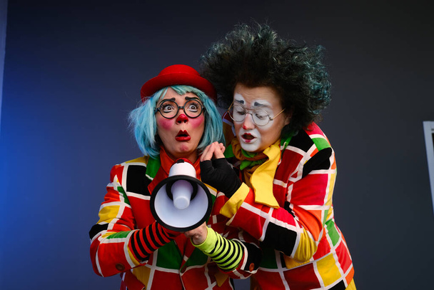 Two clowns a man and a woman with bright makeup in colored costumes speak in a megaphone to make an announcement.  - Foto, Imagem