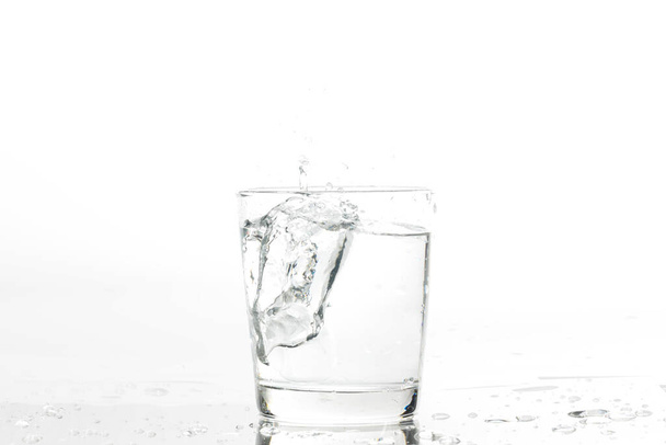 白い背景に水と氷でガラス。白い背景にミネラルウォーターと氷のガラス. - 写真・画像
