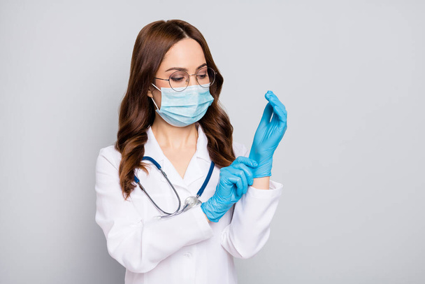 Photo of beautiful doc lady ready for operation young professional surgeon take on latex gloves wear glasses protective flu mask stethoscope white lab coat isolated grey color background - Foto, imagen