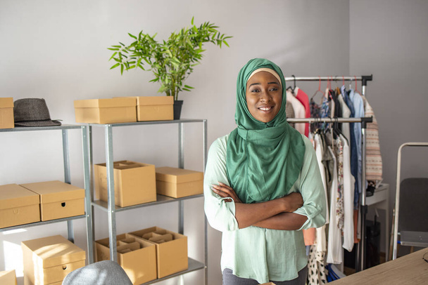 Muslim woman designer in her tailor shop. Happy smiling muslim woman designer as a startup business owner working in her tailor shop. Young women in office, looking at camera and smiling - Photo, Image