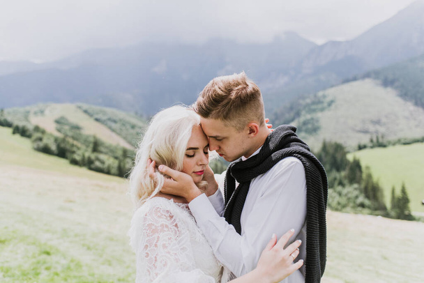 Bela noiva em um vestido estilo boho e noivo abraço e beijo nas montanhas
. - Foto, Imagem