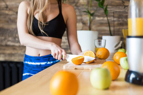 Attractive girl in sportswear preparing a healthy breakfast in the kitchen before training, cutting fruit and making fresh juice. Healthy lifestyle, fitness and beaut - Фото, зображення