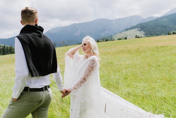 Schöne Braut und Bräutigam spazieren auf einem Feld in den Bergen. - Foto, Bild
