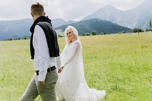 Beautiful bride and groom walk on a field in the mountains. - Photo, Image