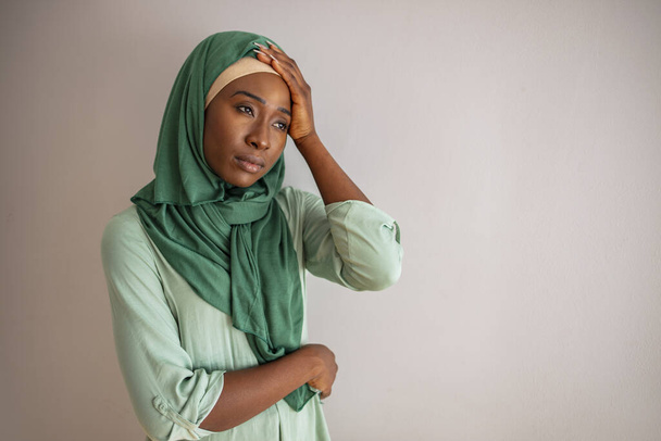 Retrato de mulher árabe pensativo em hijab em casa, descansando a cabeça nas mãos e olhando para longe com expressão facial triste, espaço cópia. Mulher muçulmana com dor de cabeça
 - Foto, Imagem