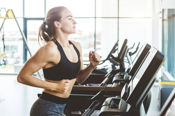 The athletic woman dressed in a black sportswear running on the treadmill in the modern gym - Foto, imagen
