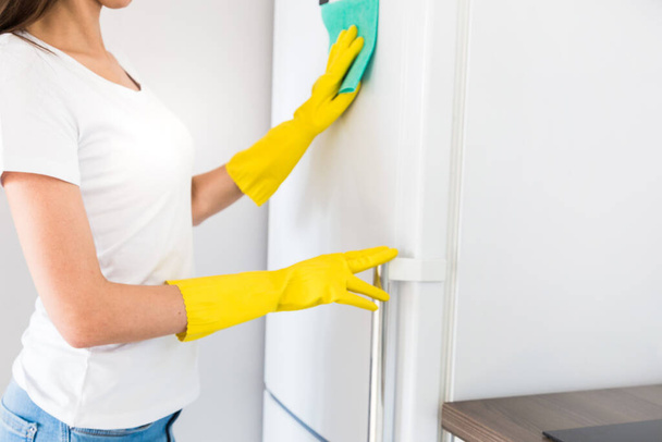 A young woman from a professional cleaning company cleans up at home. A man washes the kitchen washes the fridge in yellow gloves with cleaning supplies stuff. - Foto, afbeelding