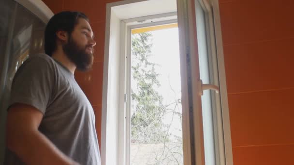 Een man in een grijs t-shirt en een baard gebruikt schoonmaakmiddel en een spons om de ramen van het huis te wassen - Video