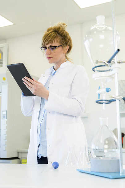 Female chemical scientist holding finger over blank tablet screen in laboratory. Healthcare pharmacy concept. - Photo, Image