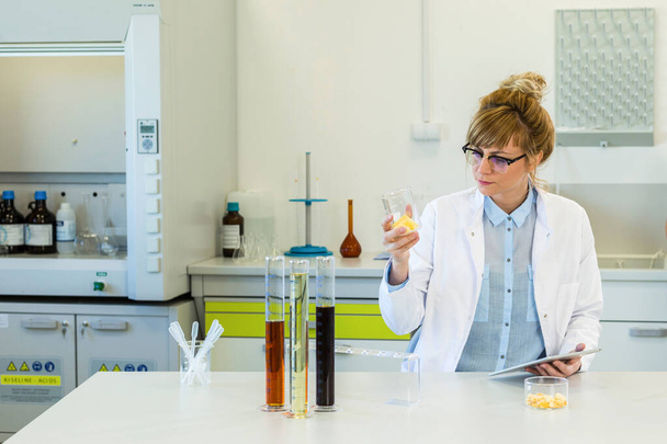 Chemikerin untersucht Hanfterpenkristalle im Labor. Sie benutzt Pinzette und Uhrglas. Auf dem Tisch liegen CBD- und CBDa-Öle und Marihuana-Samen. Gesundheitsapothekenkonzept. - Foto, Bild