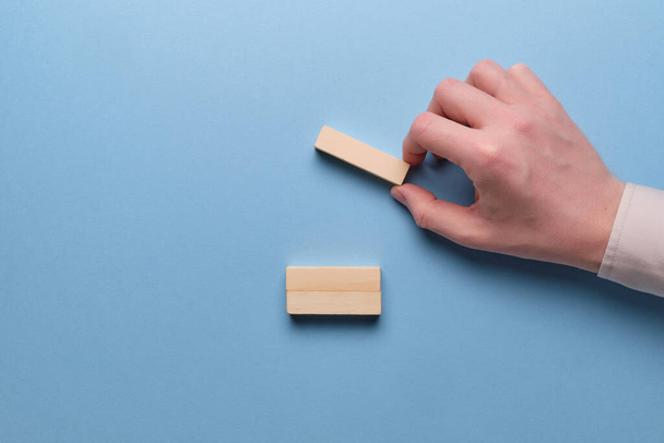 The concept of cost optimization in business. Hand holds wooden blocks on a blue background. Close up. - Foto, imagen