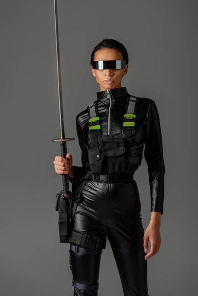attractive futuristic african american woman in glasses with sword isolated on grey - Foto, Imagem