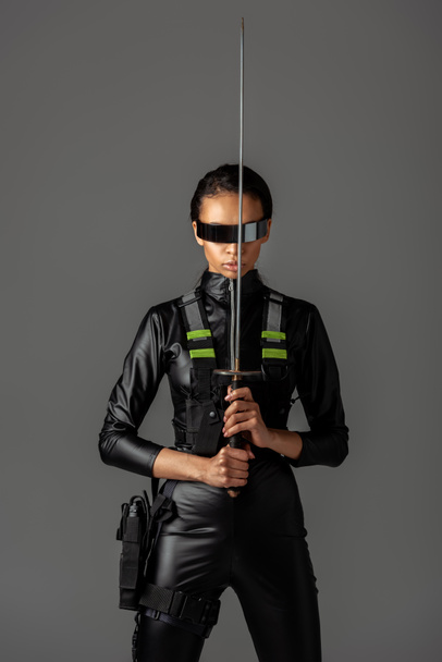 vonzó futurisztikus afro-amerikai nő szemüvegben karddal elszigetelt szürke - Fotó, kép