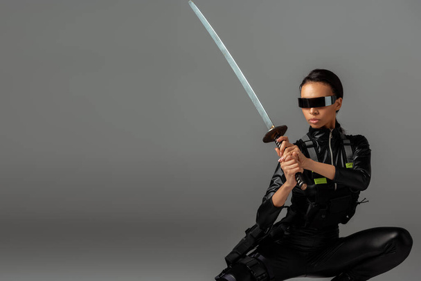 attractive futuristic african american woman in glasses sitting with sword on grey - Foto, immagini