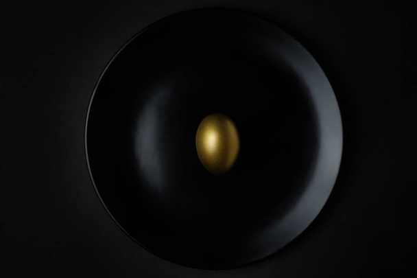Huevo dorado sobre fondo de plato negro
 - Foto, imagen