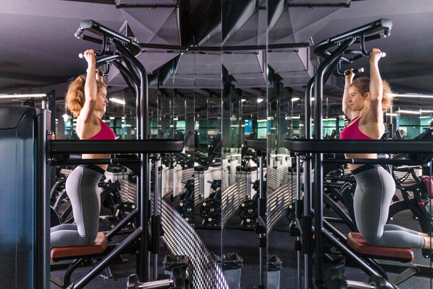 Mujer deportiva haciendo ejercicios en el aparato de entrenamiento de fuerza en el gimnasio. Levantando la barra horizontal. Gravitron Machine. Fotografía horizontal
 - Foto, imagen