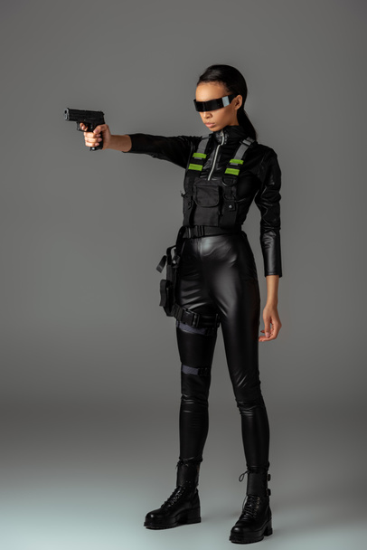 attractive futuristic african american woman in glasses aiming gun on grey - 写真・画像