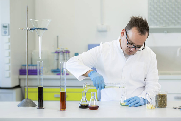 実験室で大麻CBDやCBDaの油で働く眼鏡をかけている男性化学者。彼はラテックス手袋、ガラス管とエルレンマイヤーフラスコを使用しています。大麻の種からの医療薬局. - 写真・画像