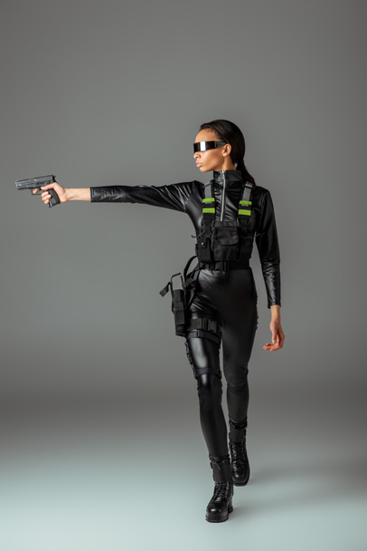 vonzó futurisztikus afro-amerikai nő szemüvegben célzás fegyvert szürke - Fotó, kép