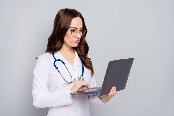 Close-up portrait of nice attractive skilled wavy-haired doc specialist phonendoscope stethoscope holding in hands laptop remote support isolated over grey pastel color background - Photo, image