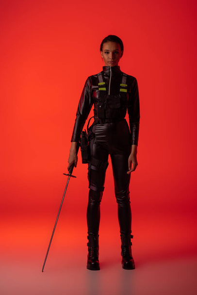 attractive futuristic african american woman in glasses with sword on red background - Photo, Image