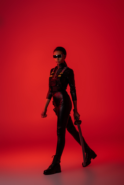 attractive futuristic african american woman in glasses with sword on red background - Foto, immagini