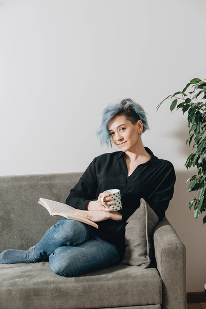 The girl with blue hair drinks tea on the couch - Zdjęcie, obraz