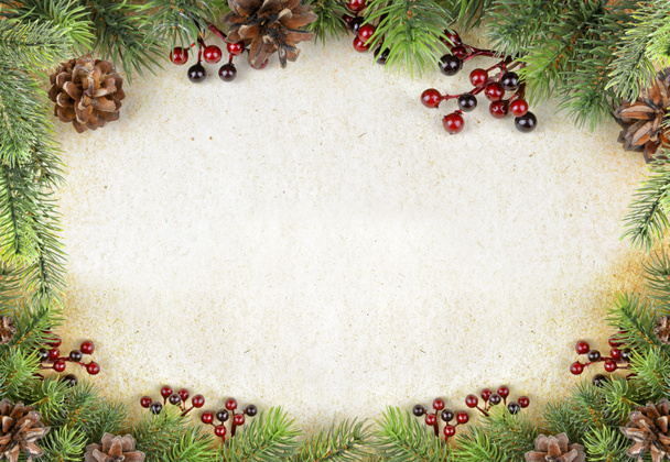 Christmas border with green fir branches, red holly berries and pine cones are on a background of old paper, with space for text - Photo, Image
