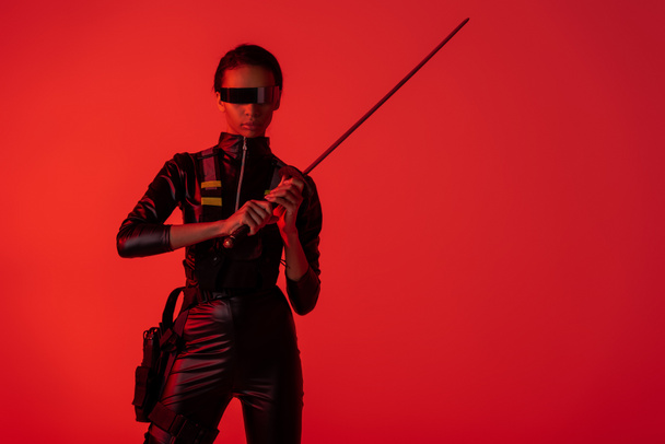 futuristische afrikanisch-amerikanische Frau in Brille mit Schwert isoliert auf rotem Hintergrund - Foto, Bild