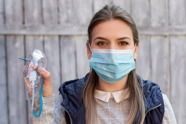 Woman wearing surgical mask is holding a medical oxygen mask outside - coronavirus pandemic - Foto, imagen