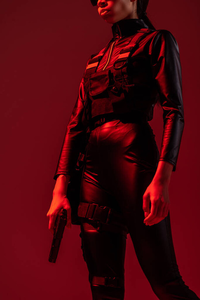 cropped view of futuristic african american woman with gun isolated on red - 写真・画像