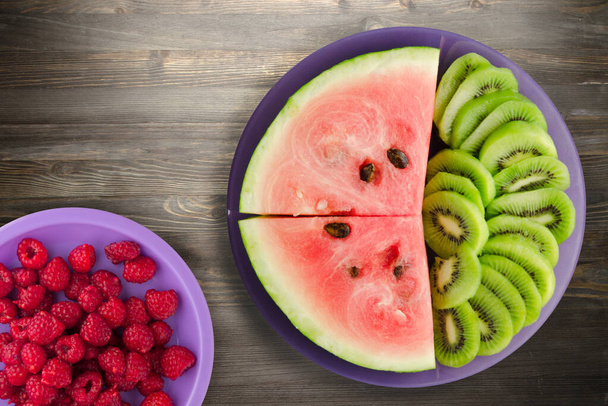 watermelon and kiwi sliced on a purple plate on a black wooden background .fruits on a plate  - Fotó, kép