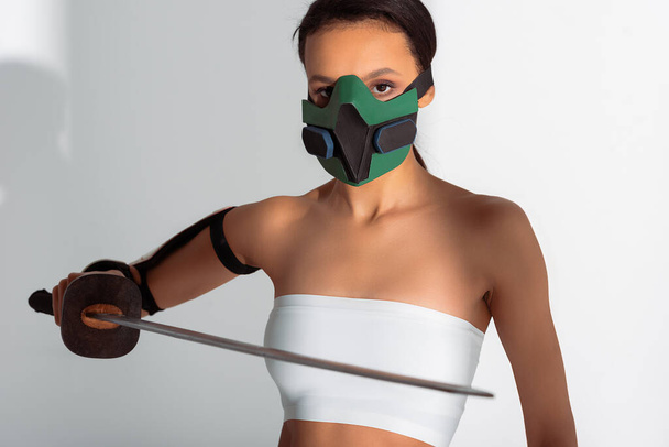 futuristic african american woman in safety mask with sword on white background - Zdjęcie, obraz