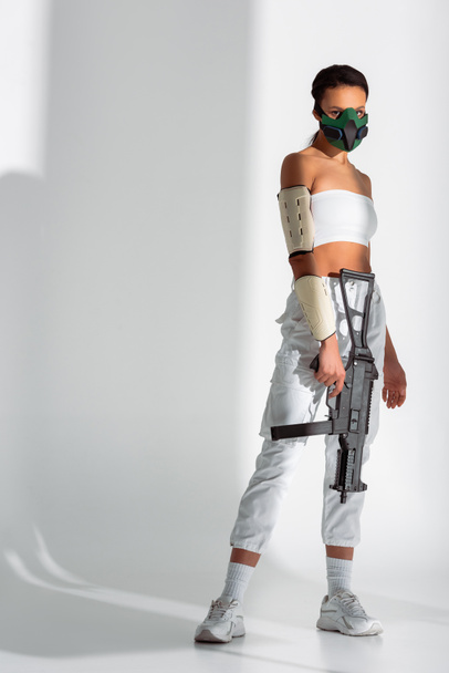 futuristic african american woman in safety mask with assault rifle on white background - Zdjęcie, obraz