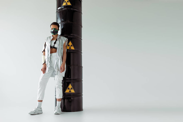 футуристическая американка в защитной маске возле бочек с радиоактивными отходами на белом фоне
 - Фото, изображение