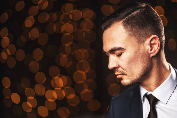 Portrait of a man in a white shirt on a dark background of bokeh garlands. Beautiful stylish portrait of a man in the room in the loft. A young Asian gentleman in the background of Christmas garlands light - Foto, Bild