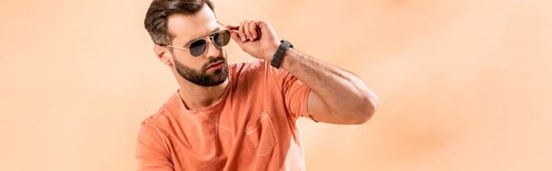panoramic shot of stylish young man posing in shorts, summer t-shirt and sunglasses on beige - Zdjęcie, obraz