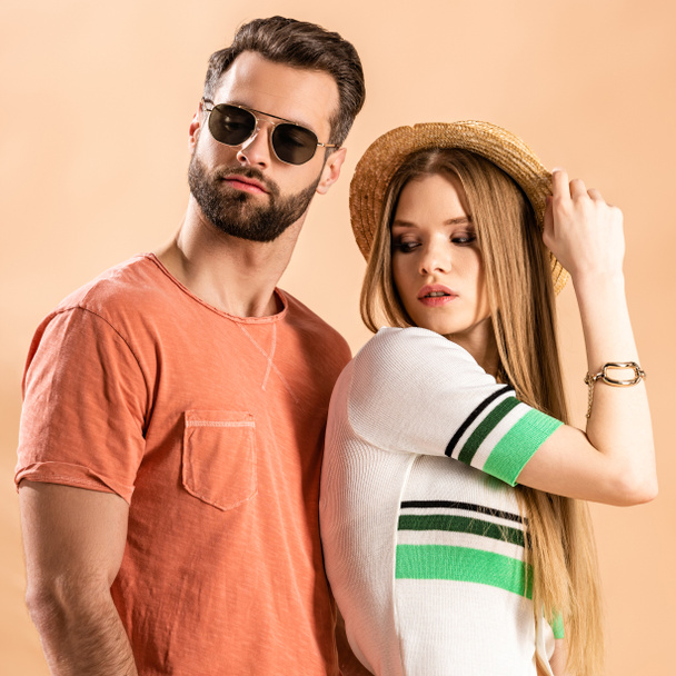 beautiful fashionable couple posing in summer clothes, straw hat and sunglasses on beige - 写真・画像