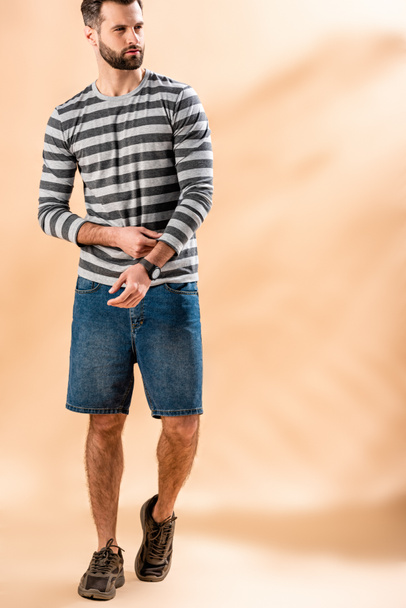 bearded young man posing in striped sweatshirt on beige - Foto, imagen