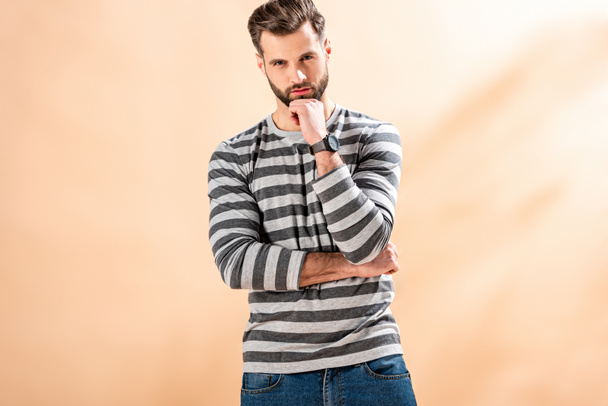 handsome bearded man posing in striped sweatshirt on beige - Zdjęcie, obraz