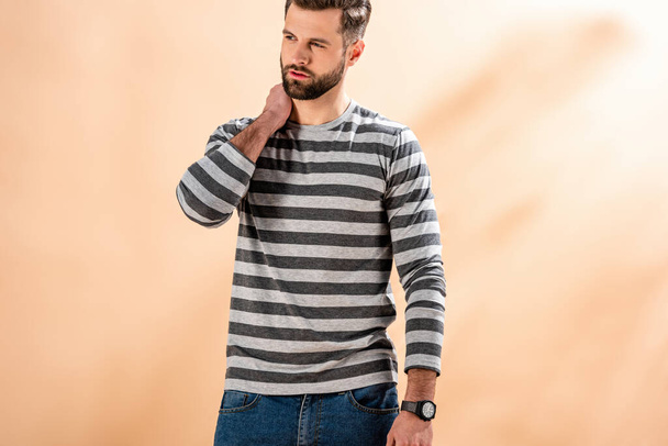 stylish bearded man posing in striped sweatshirt on beige - Photo, image