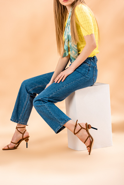 vista cortada de menina sentada em jeans, camiseta amarela, sandálias de salto alto e cachecol de seda em bege
 - Foto, Imagem