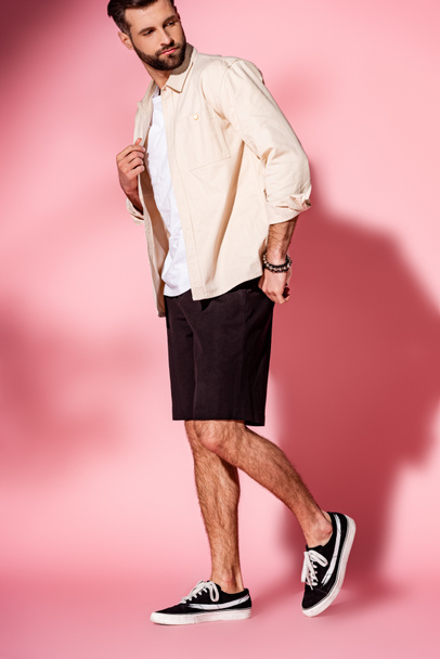 handsome bearded man posing in summer shirt and shorts on pink - Фото, зображення