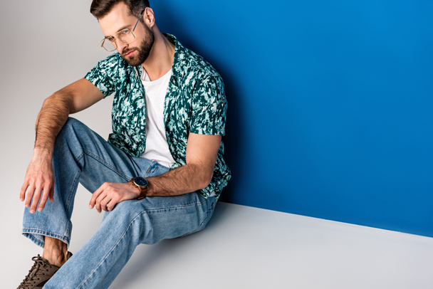 handsome bearded man posing in summer clothes and sunglasses on grey and blue - Fotó, kép