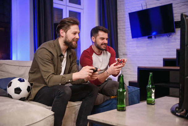 Slow motion of emotional excited funny young multiethnic guys which fooling with each other while playing video games at home ,one bearded guy celebrating victory,second getting lose - Foto, Bild