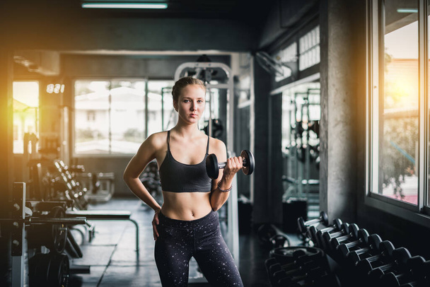 Beautiful female athletes are exercising in the gym. By lifting the dumbbell. The gym has a full range of exercise equipment. - Foto, afbeelding