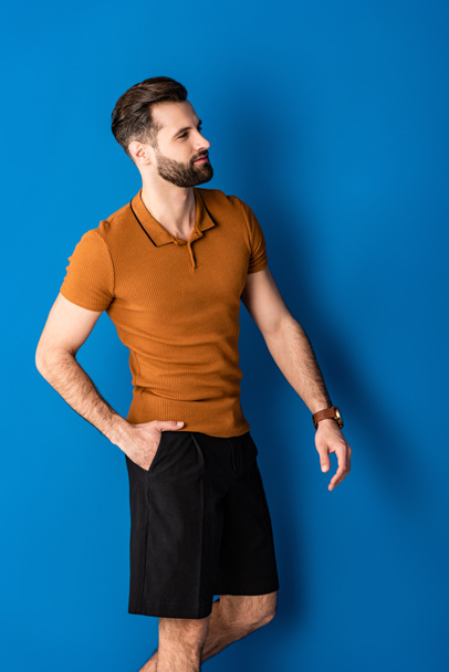 stylish positive man posing in shorts and brown polo on blue  - Фото, зображення
