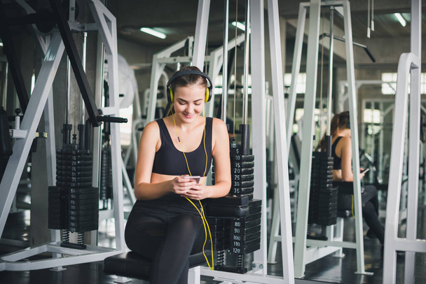 Beautiful women come to exercise in the gym and are relaxed by listening to music from headphones. She wears a sportswear. - Foto, afbeelding