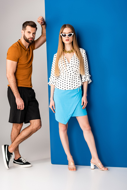 красивая пара, позирующая в летней одежде и солнечных очках на сером и синем
 - Фото, изображение